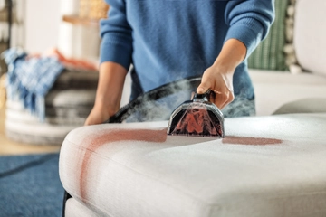 Woman cleaning stain off couch with BISSELL portable deep cleaner. 