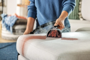 Woman cleaning stain off couch with BISSELL portable deep cleaner.