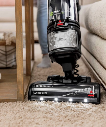 Using MultiClean Allergen Pet Slim Vacuum to vacuum carpet between chair and couch.