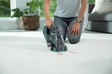 Portable deep cleaner cleaning stain off carpet.