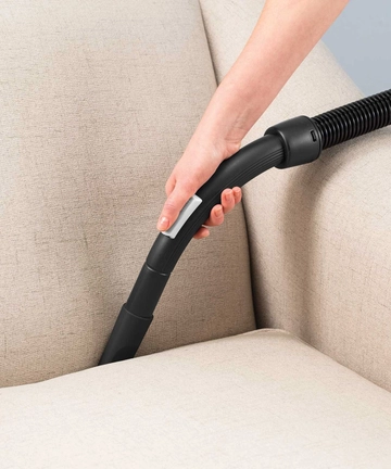 Using Hose and tool to vacuum between couch cushions.