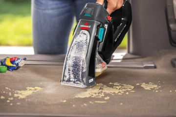 Portable deep cleaner being used to clean wet stain off car upholstery. 
