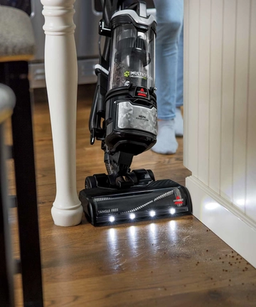 MultiClean Allergen Pet Slim Vacuum vacuuming hard flooring along baseboard with headlight feature.