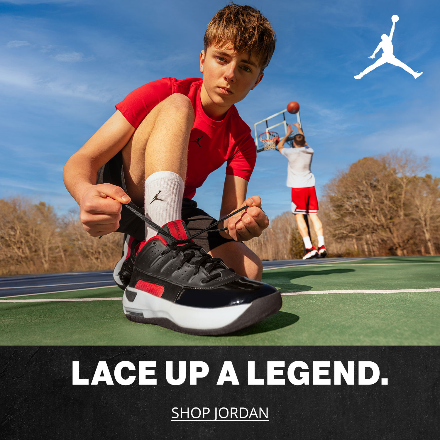 A teenage boy tying his Jordan Brand basketball shoes on a basketball court outside while a friend shoots a ball towards the hoop in the background.	Lace up a Legend.