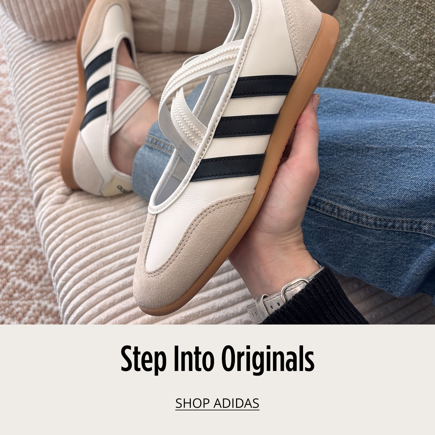 Hand holding one athletic adidas sneaker by laces in air with matching shoe on floor on green background