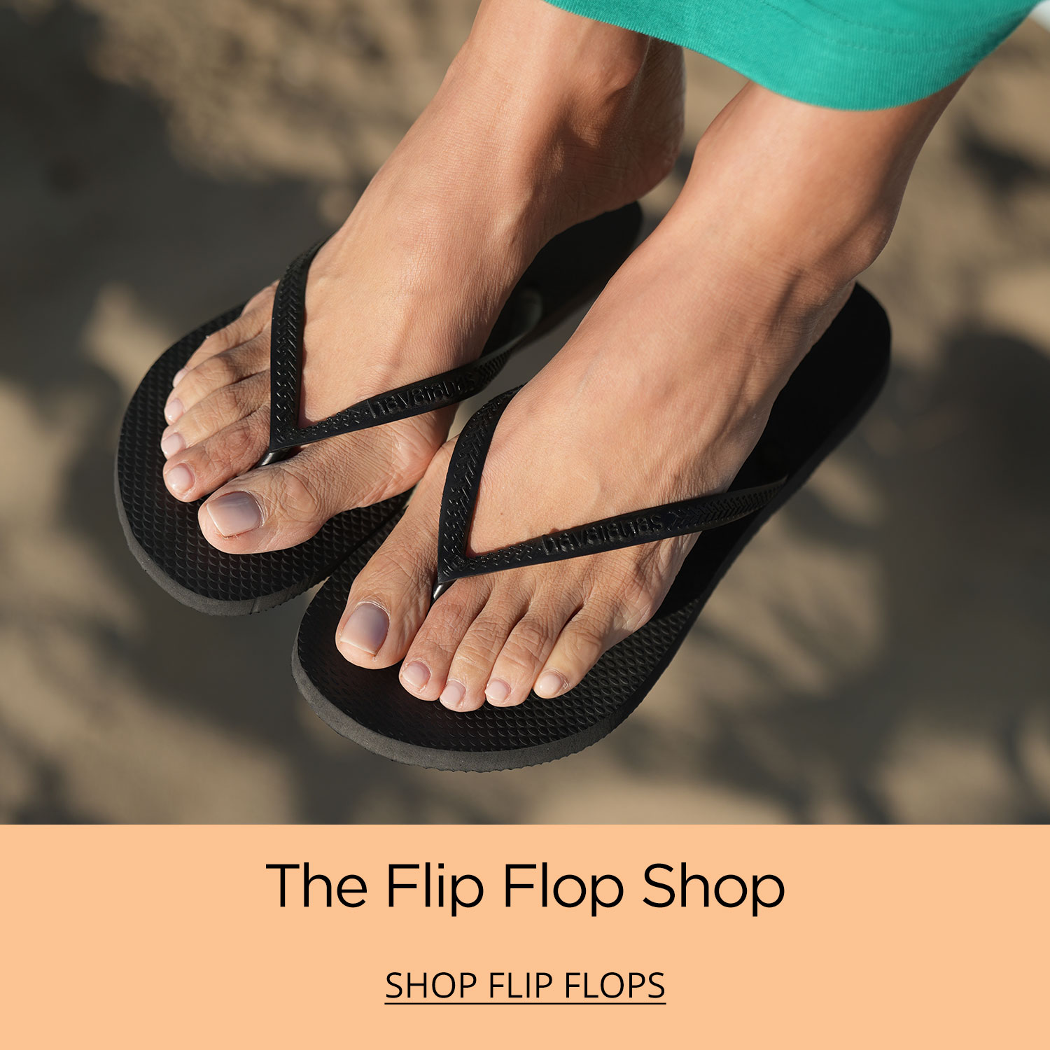 Woman's feet wearing black Havaianas Slim style flip flops against a sandy beach background