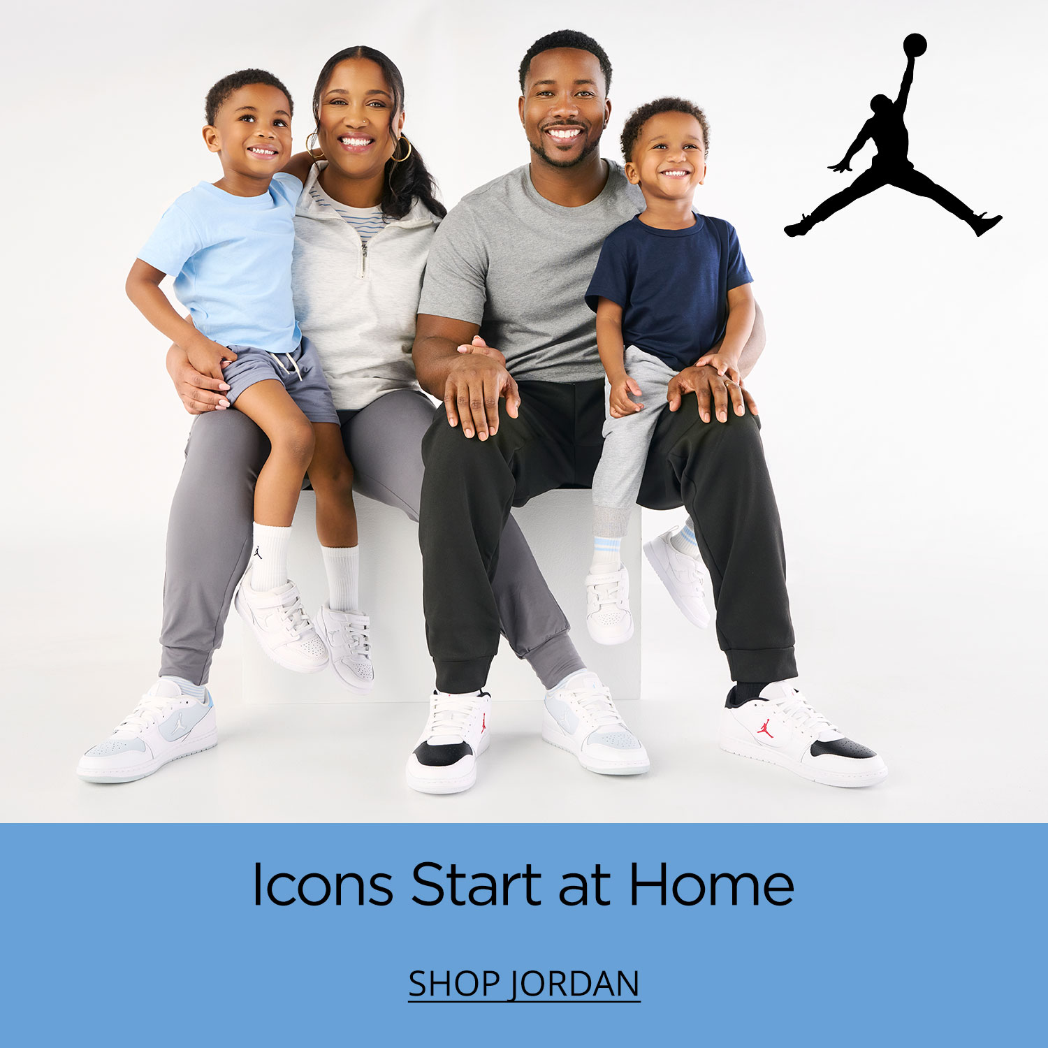A family of four, mom, dad and two young boys smilng sitting on a shared plinth wearing trendy new Jordan sneakers.