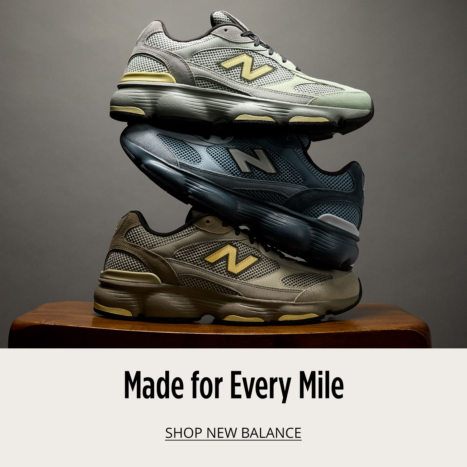 Three attractive New Balance athletic sneakers are placed on table and are stacked on top of each other vertically on grey background