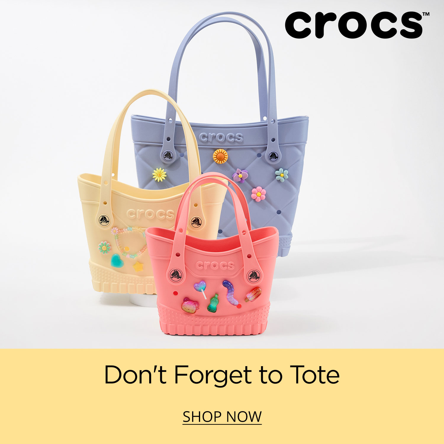 Assorted Crocs tote bags accessorized with Jibbitz sitting on white background. Don't forget to tote. Crocs logo at top of image.