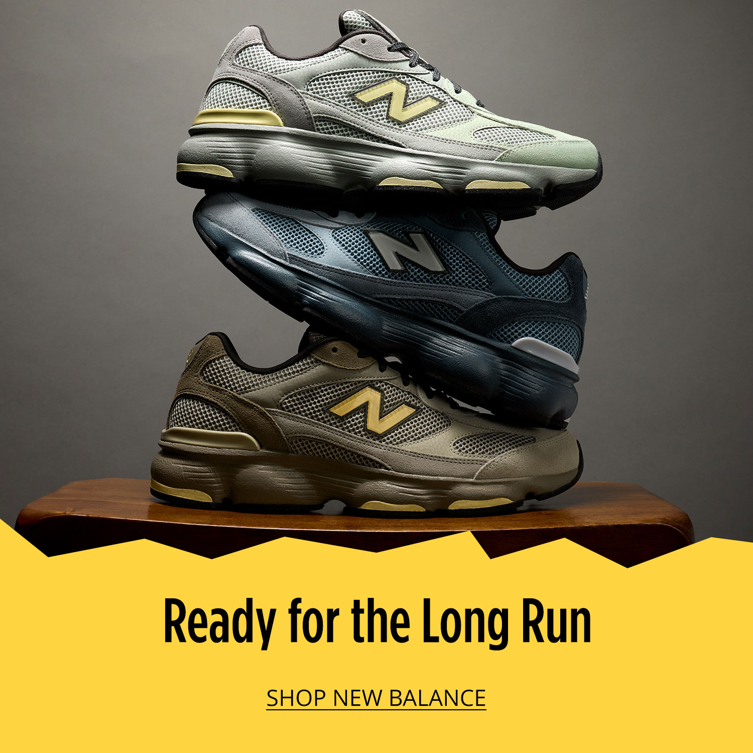 Three attractive New Balance athletic sneakers are placed on table and are stacked on top of each other vertically on grey background