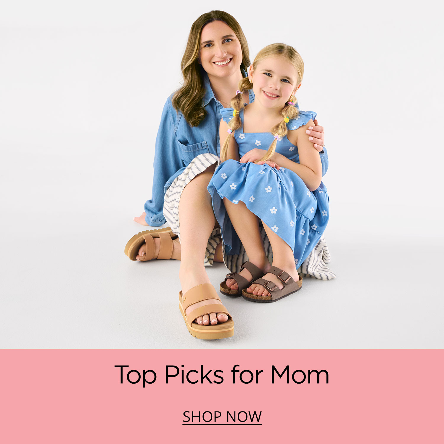 A mom and her young daughter sitting together on the ground wearing comfortable stylish sandals perfect for summer.