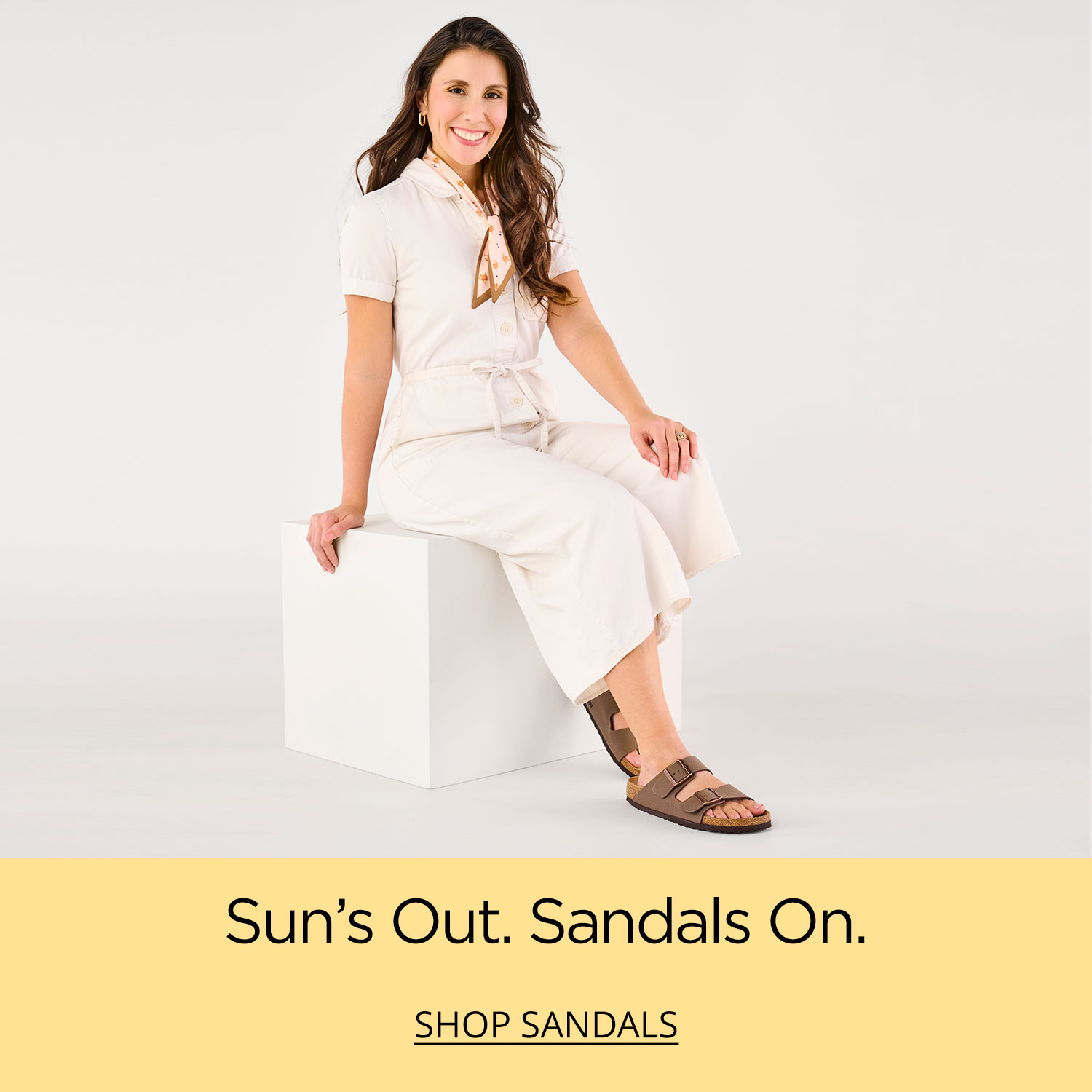 A mom smiling whiling sitting on a white box wearing comfy and durable Birkenstock Arizona sandals.