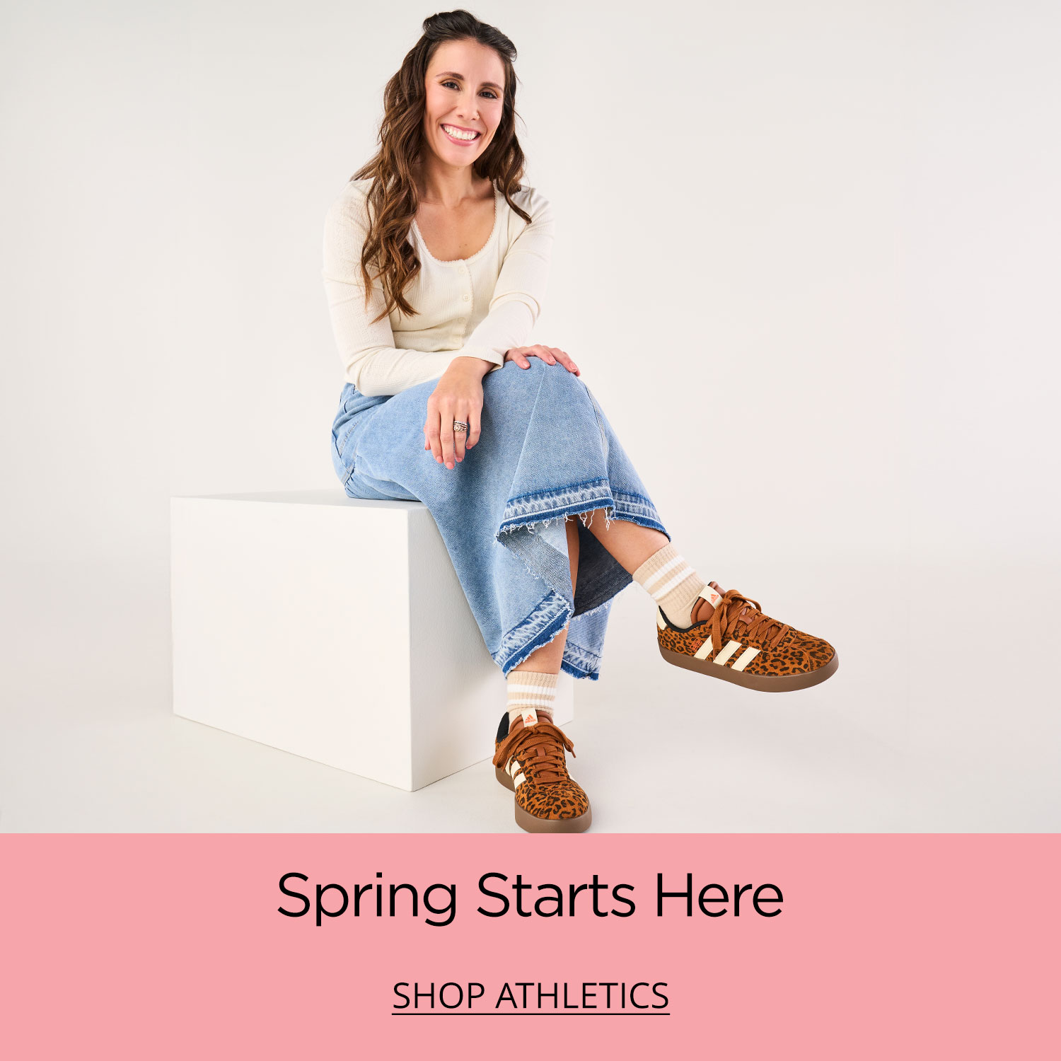 A stylish mom sitting on a white box wearing her leopard print adidas VL Court 3.0 sneakers.