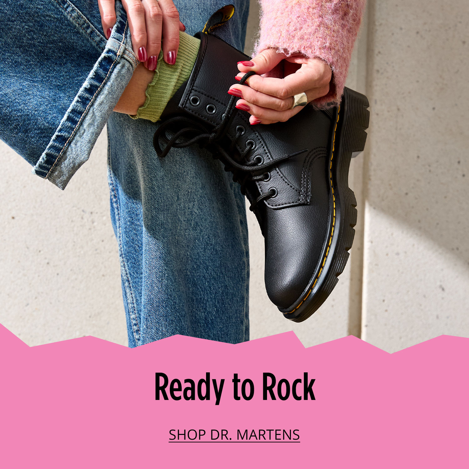 Woman lacing Dr. Martens boots styled with blue pants and pink top			