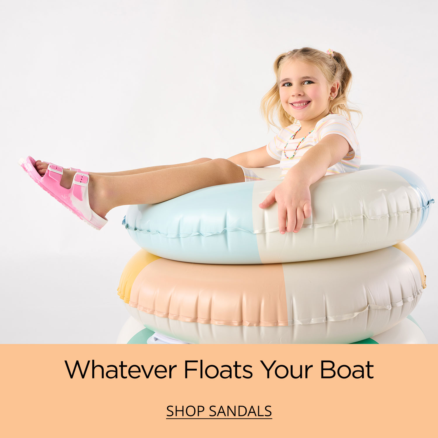 A young girl about to enjoy a pool day sitting on top of three floats wearing her favorite sandals.