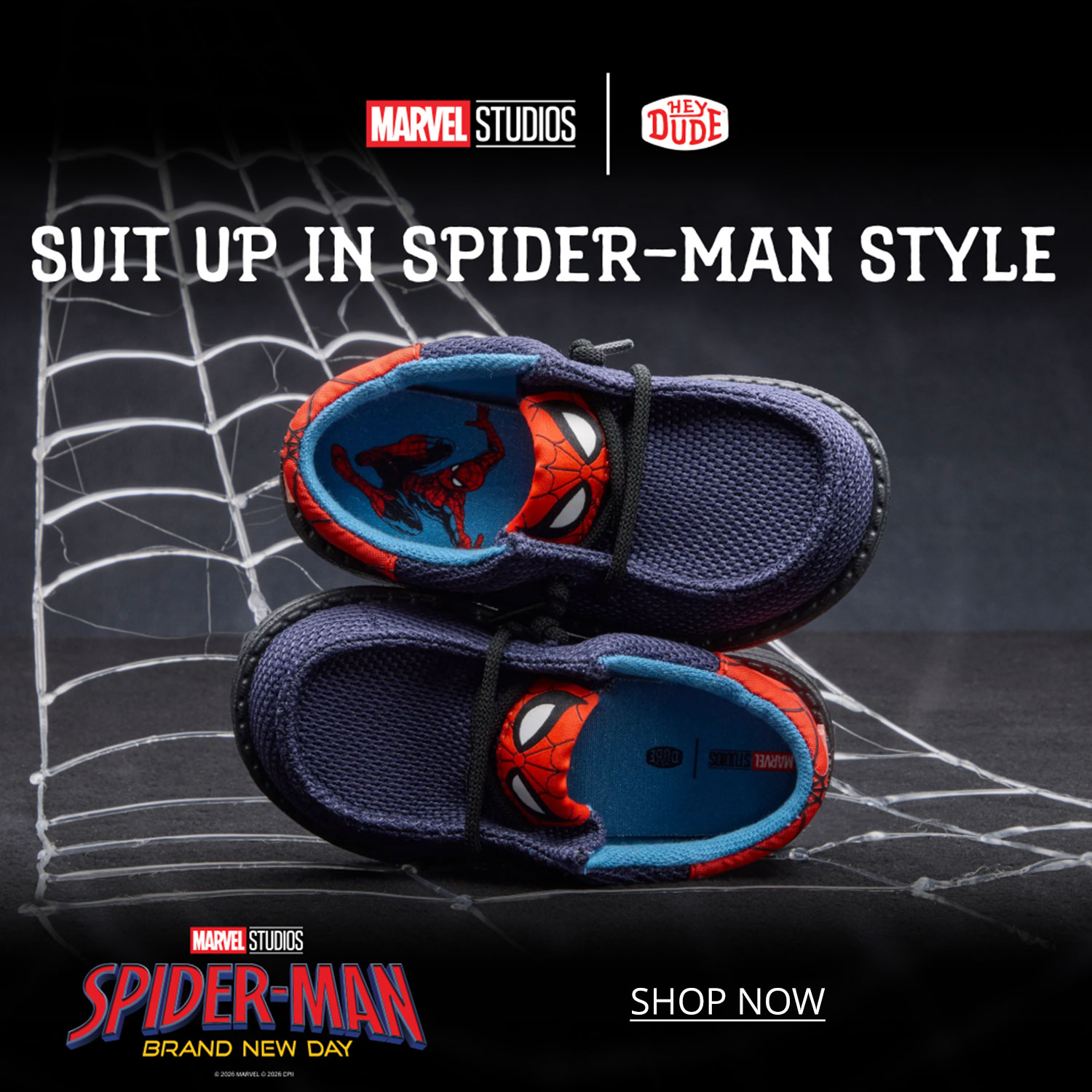 A pair of kids' Marvel Studios Spiderman themed Heydude slip-ons, sitting on a black table with a spider web in the background.