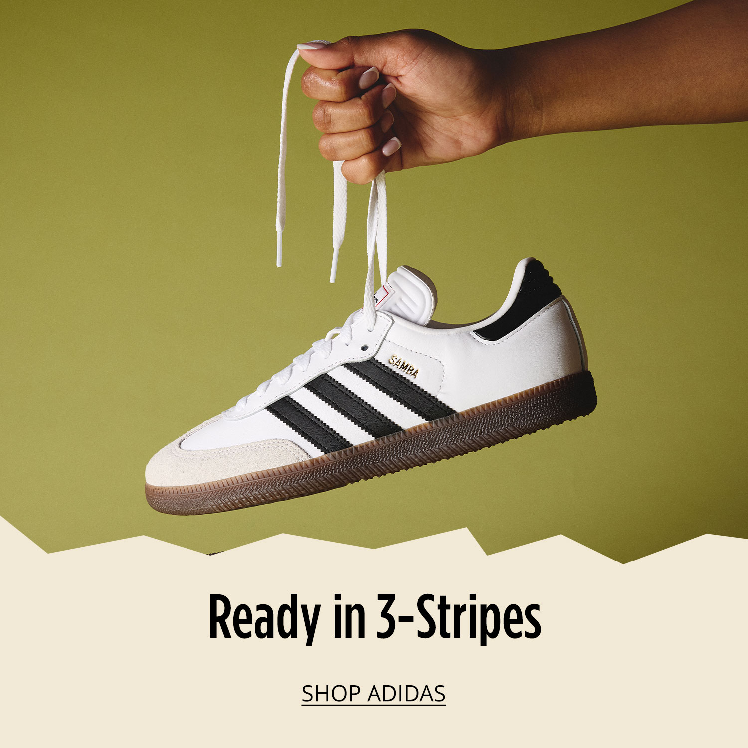 Hand holding one athletic adidas sneaker by laces in air with matching shoe on floor on green background