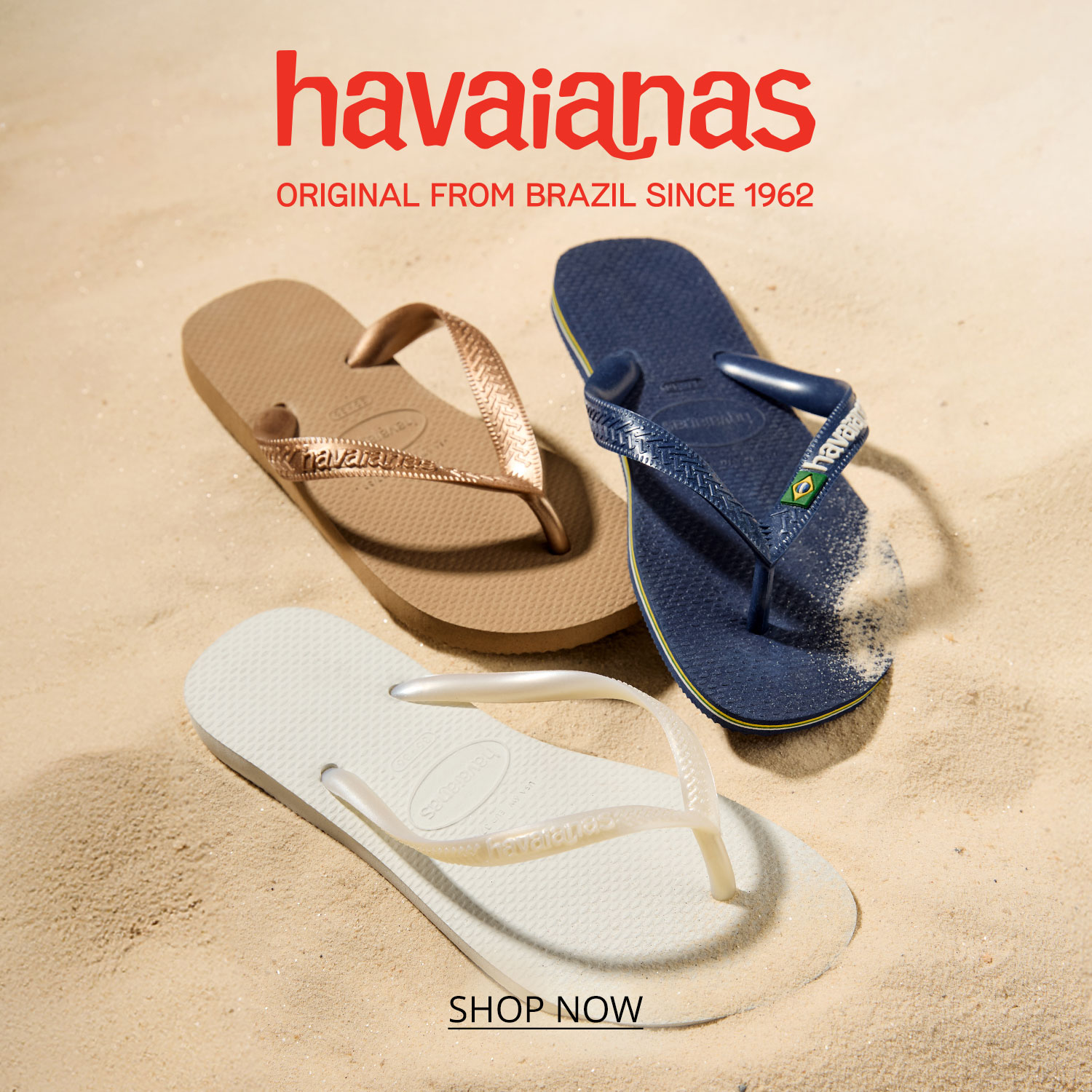 A lifestyle shot of a number of items including a pair of black Haviana flip flops, a sun hat, sunglasses, a book and beach bag on top of a yellow beach blanket at the beach.