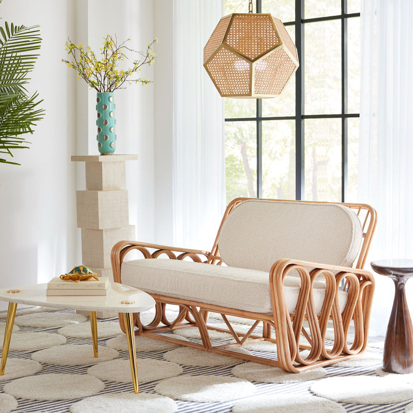 A curved wooden frame settee with a light-colored cushion and backrest, accompanied by a small white table and geometric hanging lamp.