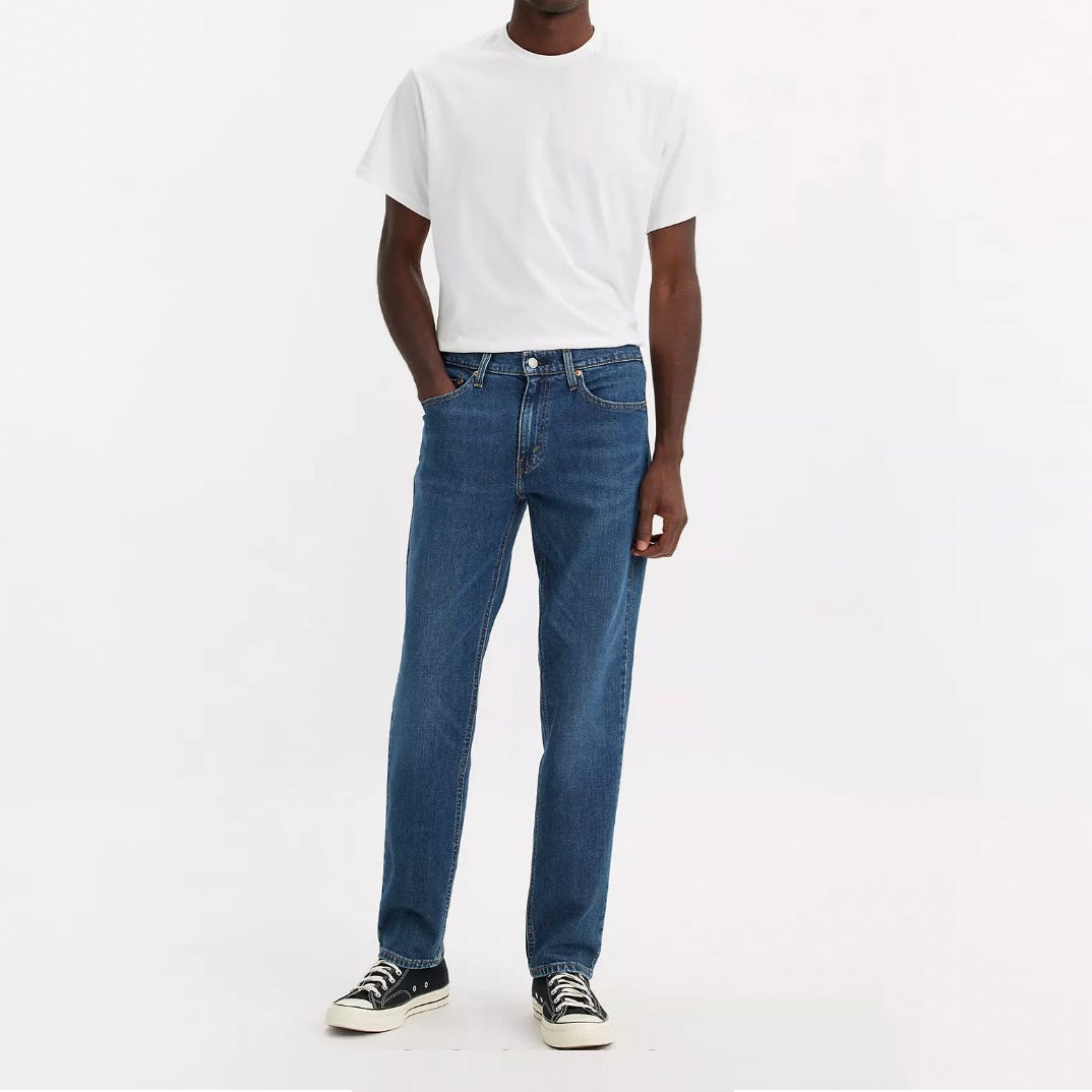 A man is wearing a plain white t-shirt, blue jeans, and black and white sneakers.
