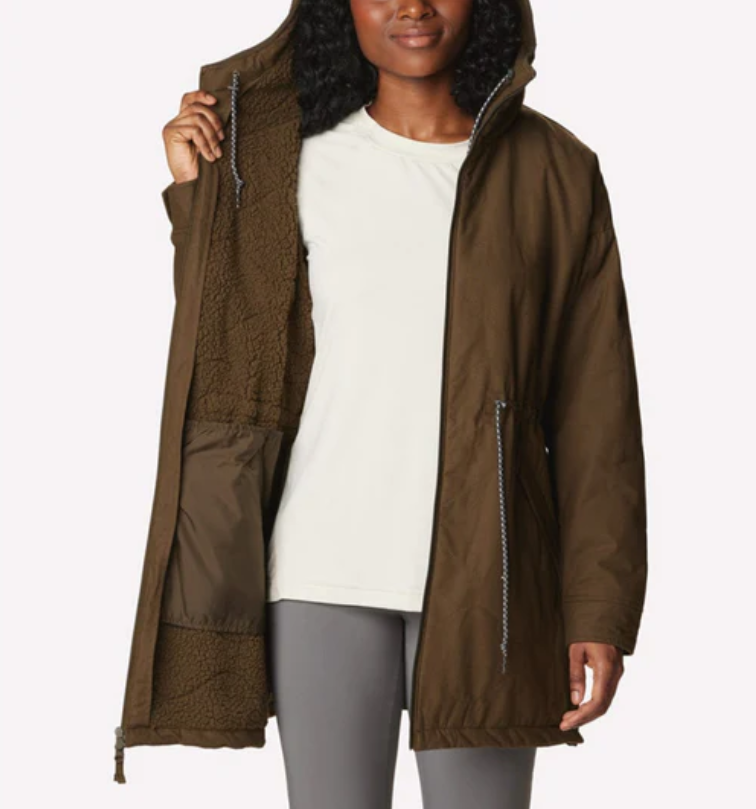 A woman is wearing a brown hooded parka with a zippered side pocket and a white T-shirt, paired with grey leggings.