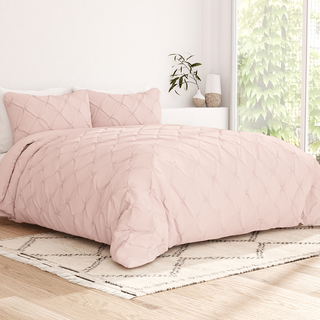 A pink quilted duvet cover and matching pillowcases on a bed, with a beige patterned rug underneath.
