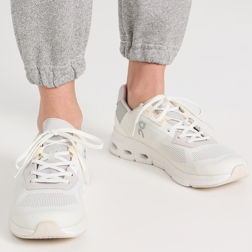 Light grey and white sneakers with a breathable mesh upper and unique cushioned outsole. They have a low-top design and white laces.