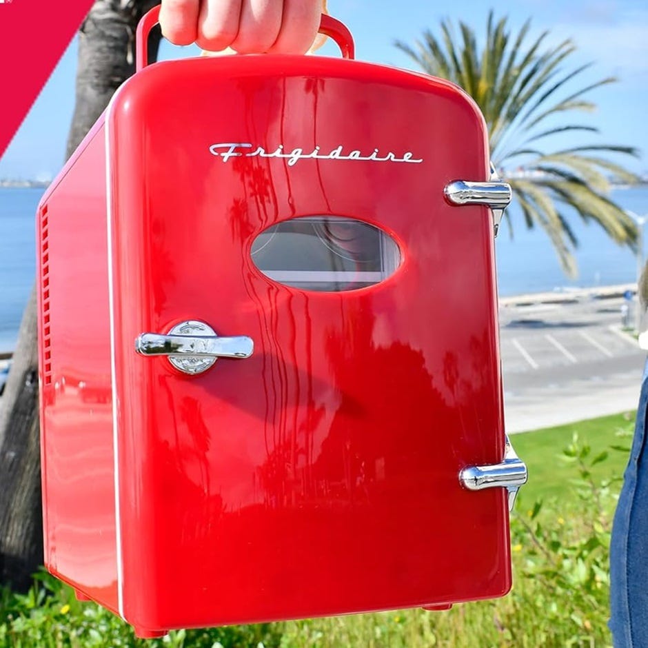 A red Frigidaire portable mini-fridge with a clear window held by someone outdoors.