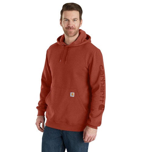 A man is wearing a red Carhartt hoodie with the brand name on the sleeve and a small logo on the pocket, paired with jeans.