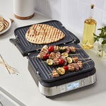 A Cuisinart Griddler is shown with grilled flatbread on the top plate and skewers with meat and vegetables on the bottom.