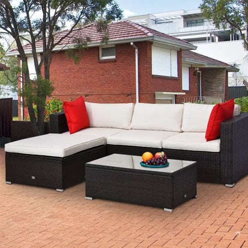 An outdoor sectional sofa with white cushions, a chaise, and a glass-topped coffee table with a bowl of fruit.