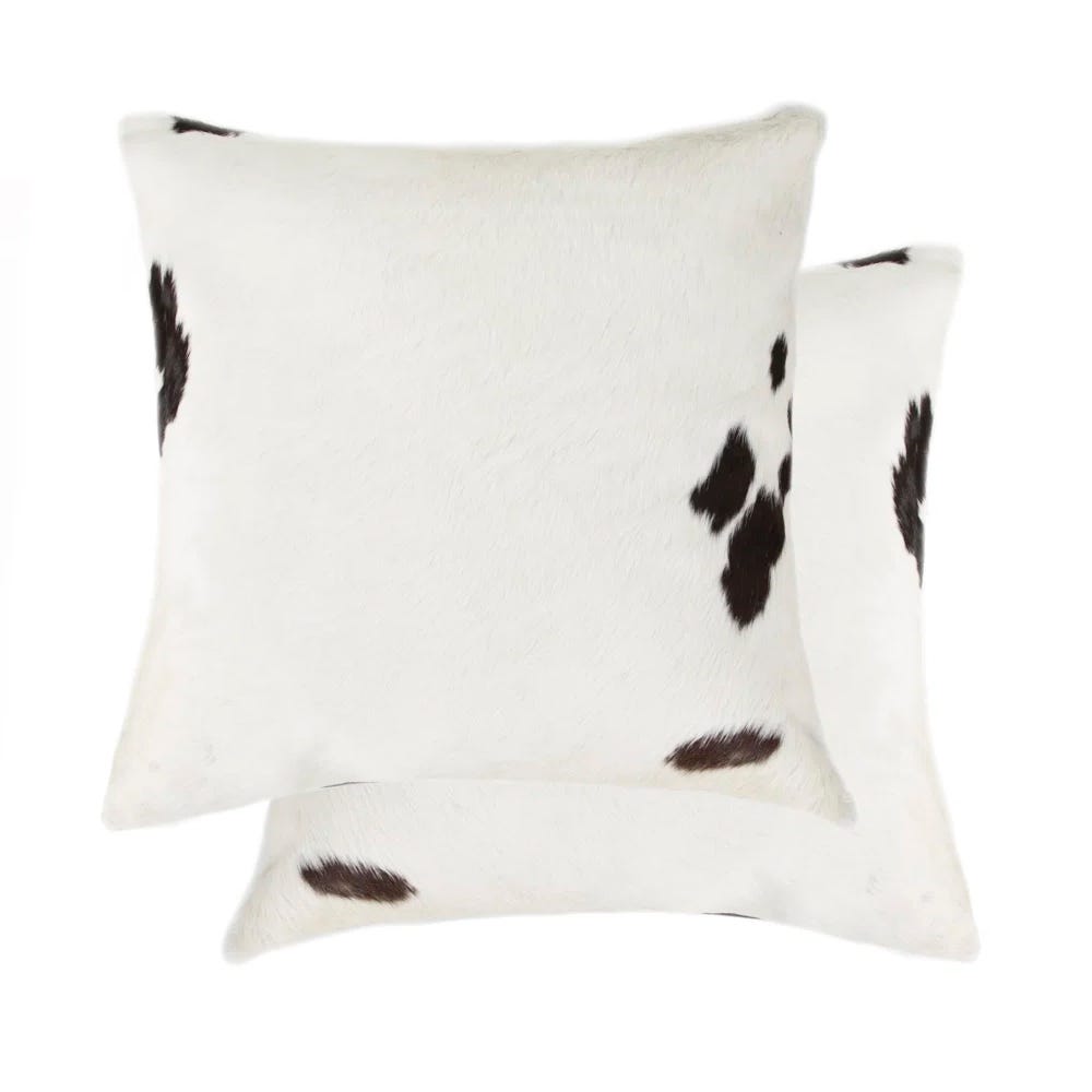 Two square cowhide-patterned pillows with a white base and dark brown spots.