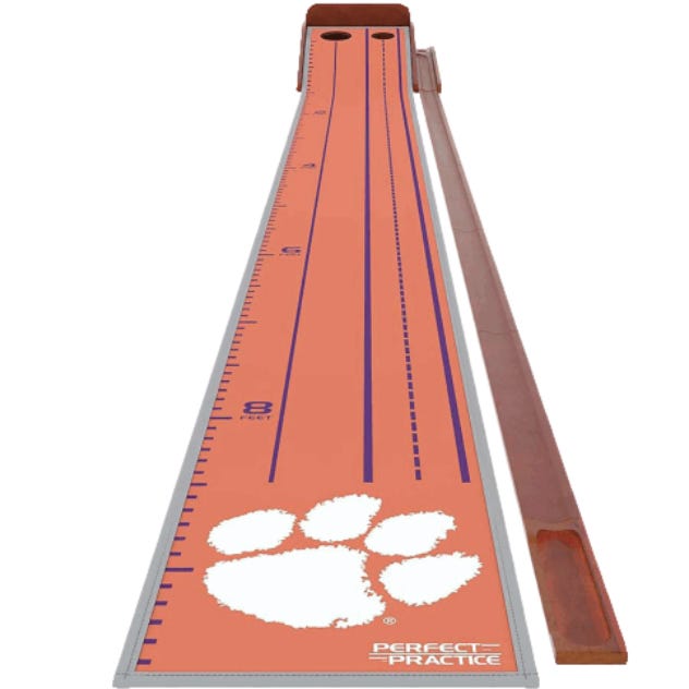 The Collegiate Golf Putting Mat is an orange practice mat with blue alignment lines and a white paw logo, suitable for improving golf putting skills. It features distance markings up to 8 feet and includes a wooden ball return system.