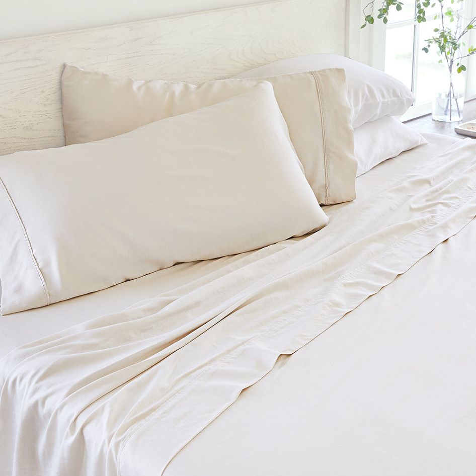 Linen-Bamboo Cooling Sheet Sets feature soft, cream-colored sheets with a natural drape and smooth texture, designed for breathability. They include pillowcases and a fitted sheet, ideal for keeping cool and comfortable while sleeping.