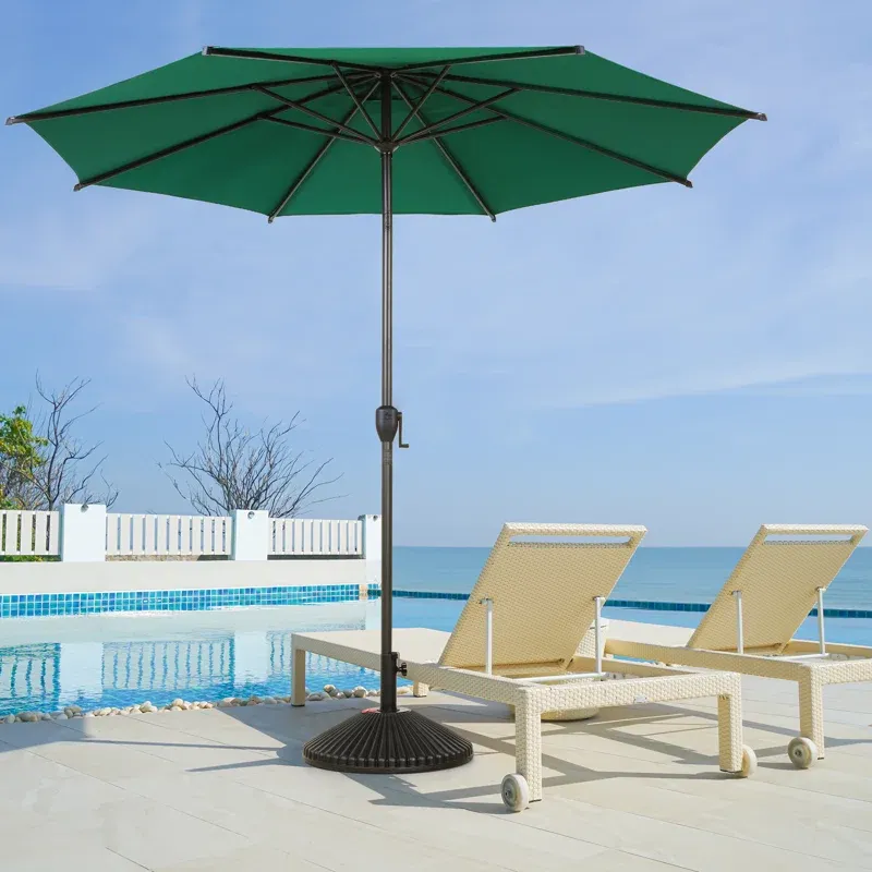 Two beige sun loungers under a large green patio umbrella by a poolside, overlooking the sea.