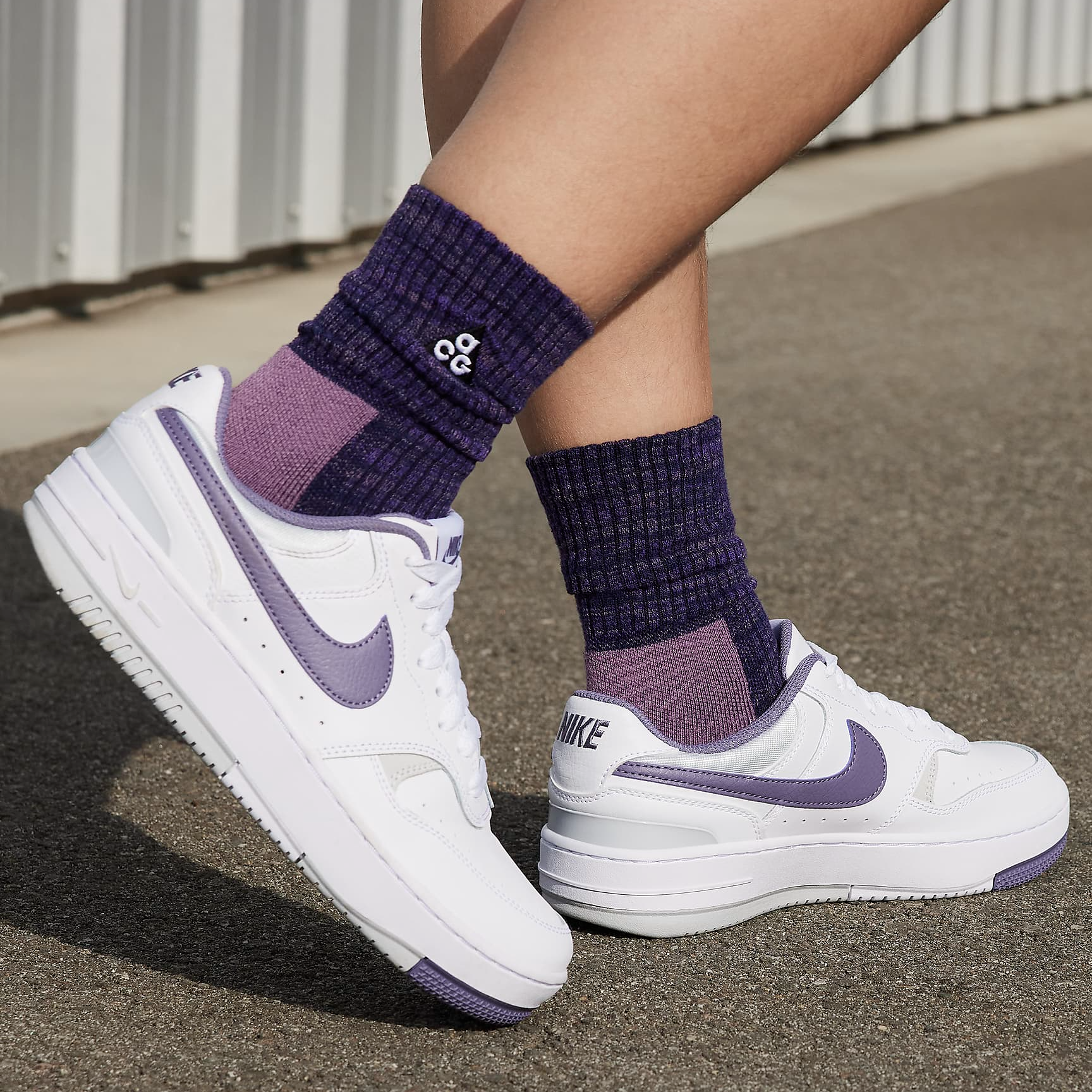 A pair of white Nike sneakers with purple accents and matching purple crew socks.