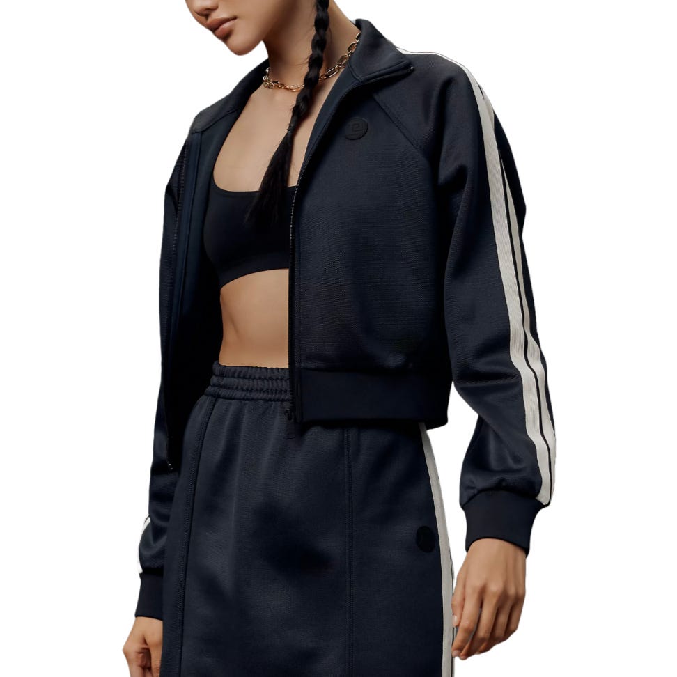 A woman models a black tracksuit with white stripes, comprising a cropped zip-up jacket, sports bra, and high-waisted pants.