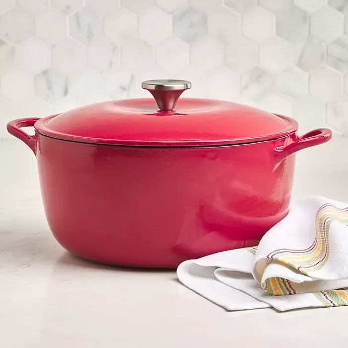 A red enameled cast iron Dutch oven with a lid, beside a striped kitchen towel.