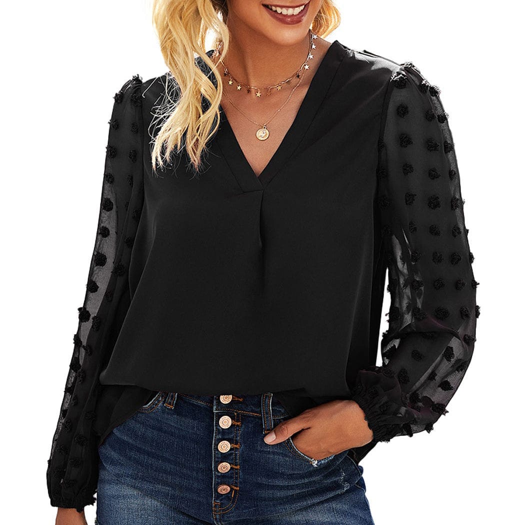 A woman wearing a black V-neck blouse with sheer sleeves and decorative accents, paired with blue jeans.