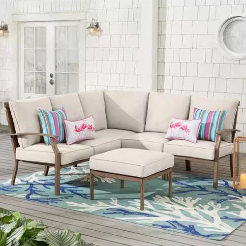 An outdoor sectional sofa with beige cushions and a matching ottoman on a blue and white patterned rug.