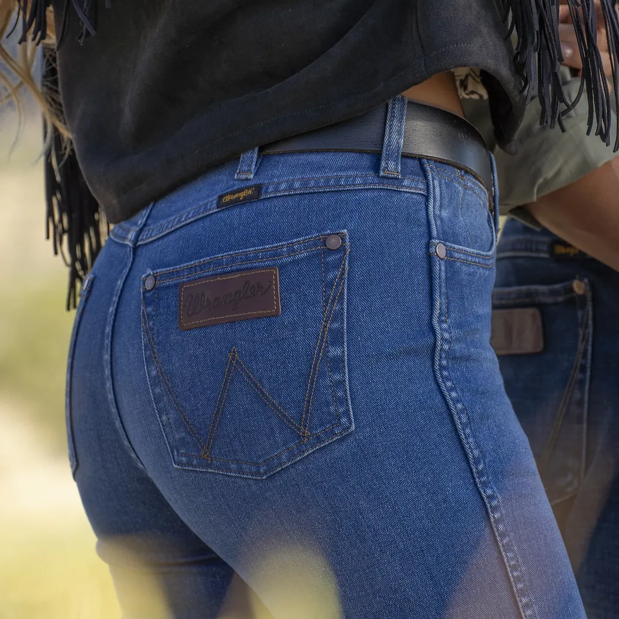A person wearing blue denim Wrangler jeans with a branded leather patch on the back pocket.