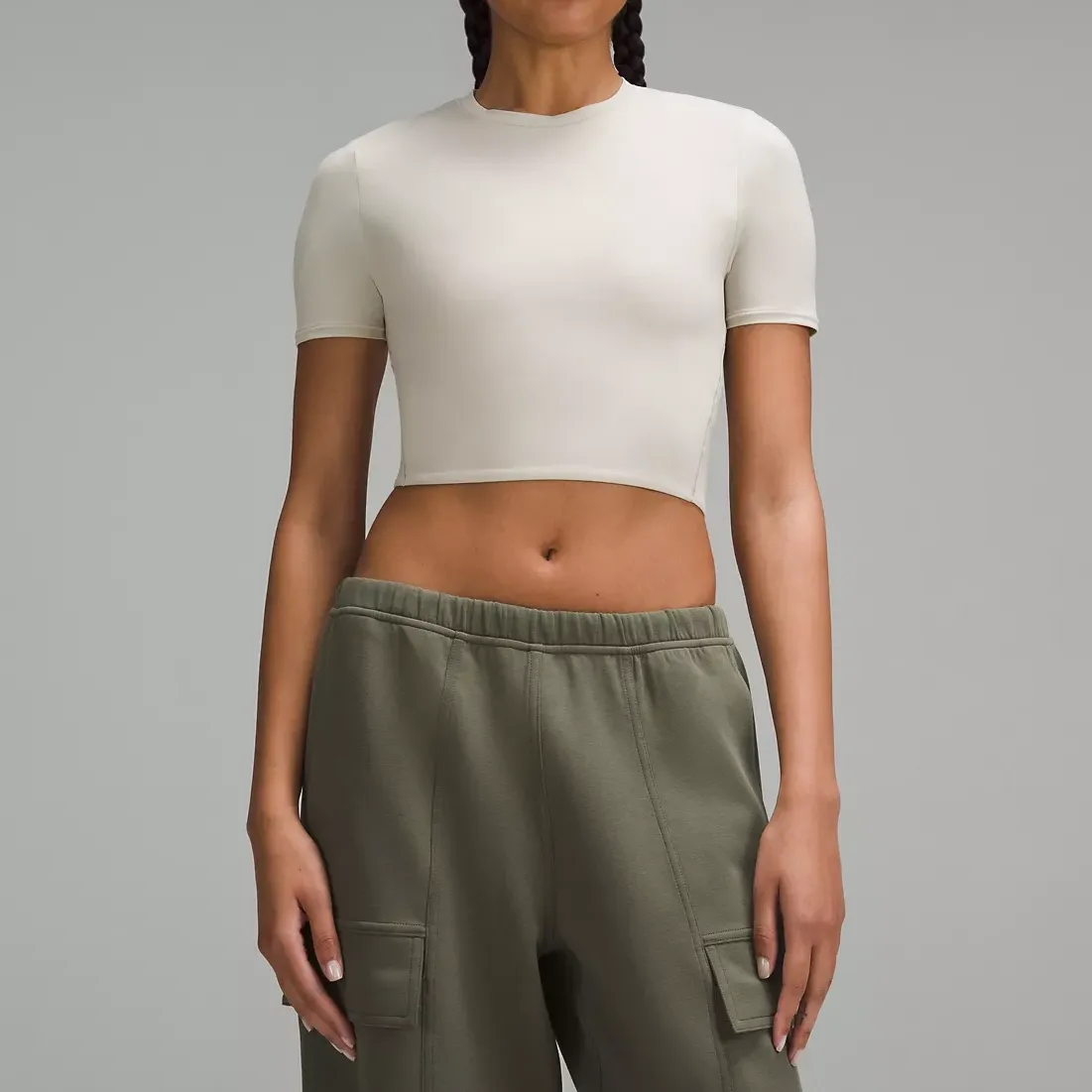 A woman is wearing a white crop top and olive green cargo pants.