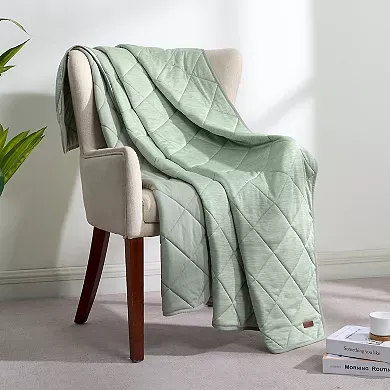 A quilted blanket in a soft green color is draped over a cream-colored chair, featuring a diamond pattern.