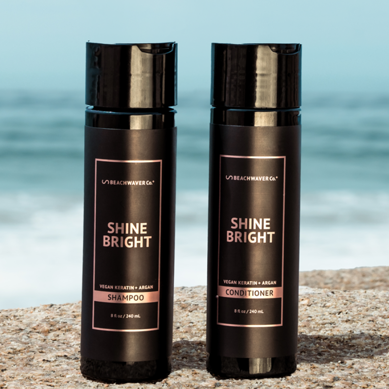 Beachwaver Co. Shine Bright Shampoo and Conditioner, featuring vegan keratin and argan, each in an 8 oz (240 mL) bottle, set against a beach backdrop.