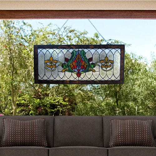 Stained glass window hanging with a colorful floral design above a gray sofa.