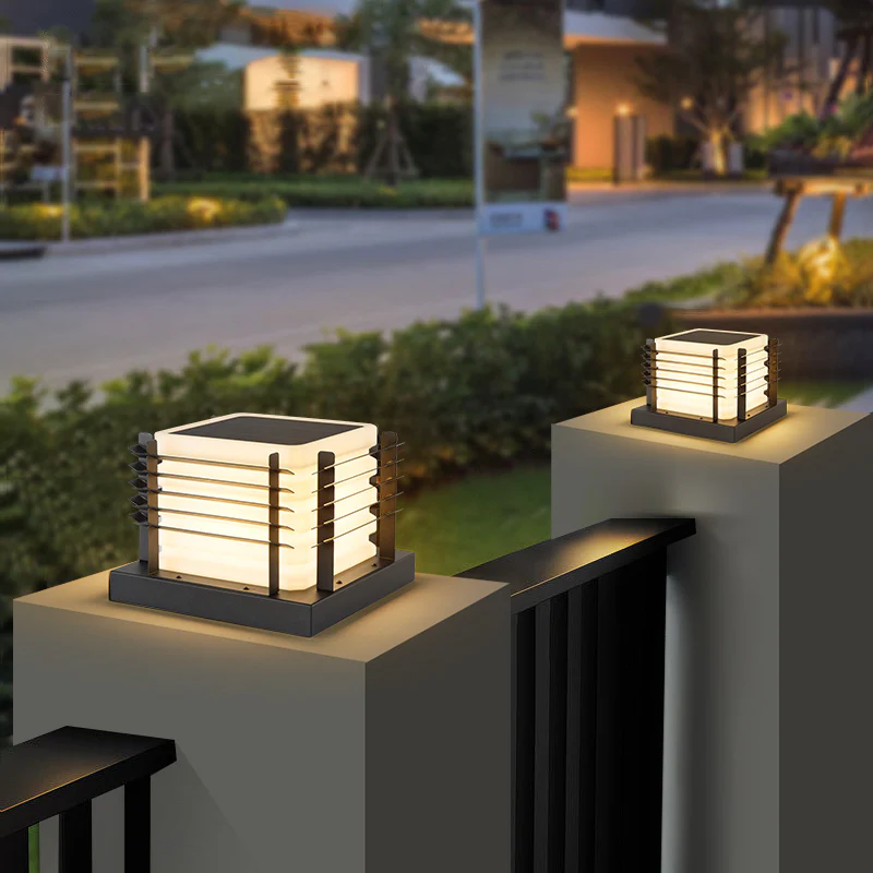 Two square-shaped solar LED pillar lamps with slatted metal sides are mounted on top of posts, providing outdoor lighting.