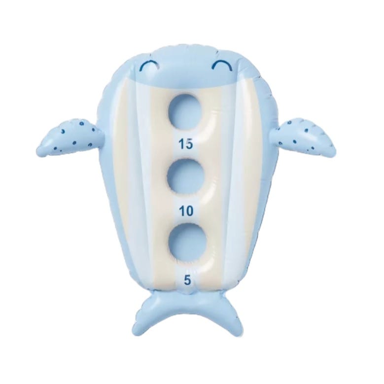 Inflatable whale-shaped beanbag toss float with three holes labeled 5, 10, and 15. It has small fins and a tail, a smiling face, and is light blue with beige stripes. Suitable for pool games and activities.