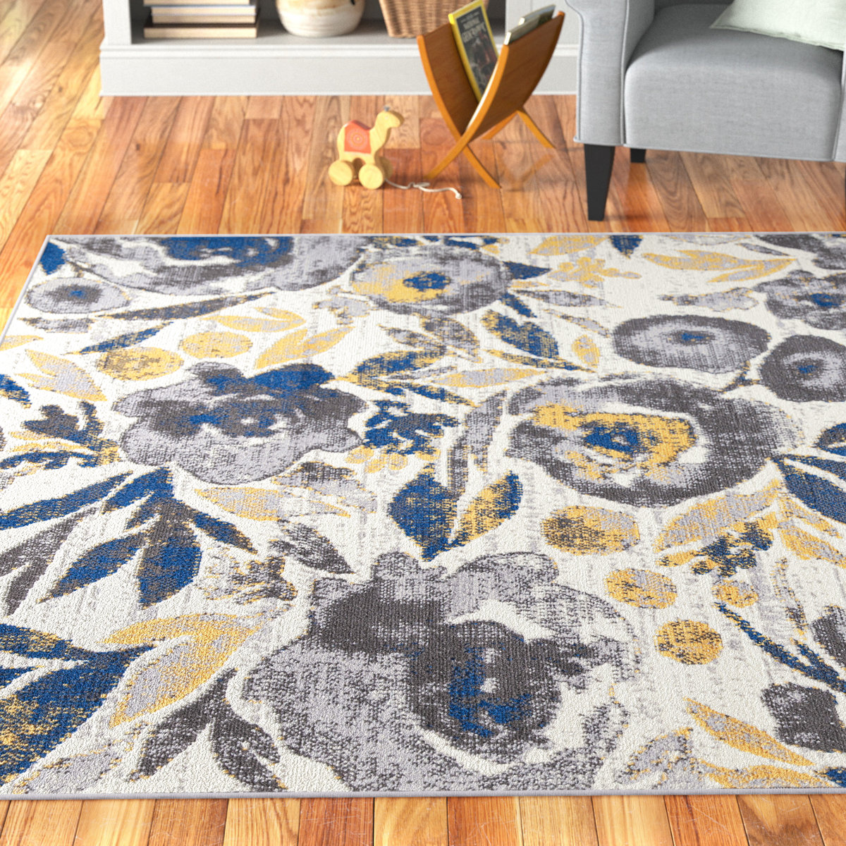 An 8' x 10' floral area rug with a pattern of large gray, blue, and yellow flowers on a light background, placed on a wooden floor in a cozy living room setting.