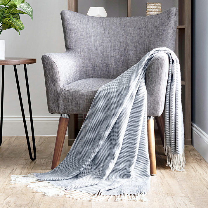 A gray upholstered armchair with wooden legs and a light gray herringbone-patterned throw blanket.