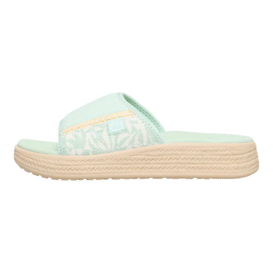 A mint green slide sandal with a textured sole and light beige platform, featuring a strap with a subtle pattern and yellow detailing.